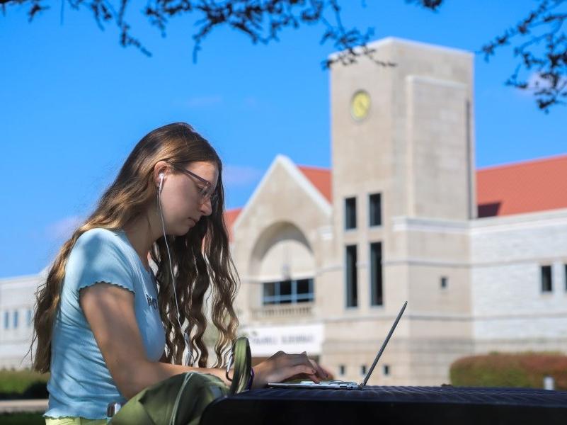 College student sitting outside library, working on laptop computer